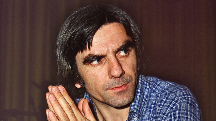 Das Bild zeigt den Soziologen und ehemaligen Studentenführer Rudi Dutschke, ein dunkelhaariger Mann mit blau-kariertem Hemd. 