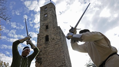 Zwei Ritter duellieren sich vor einer Burg.