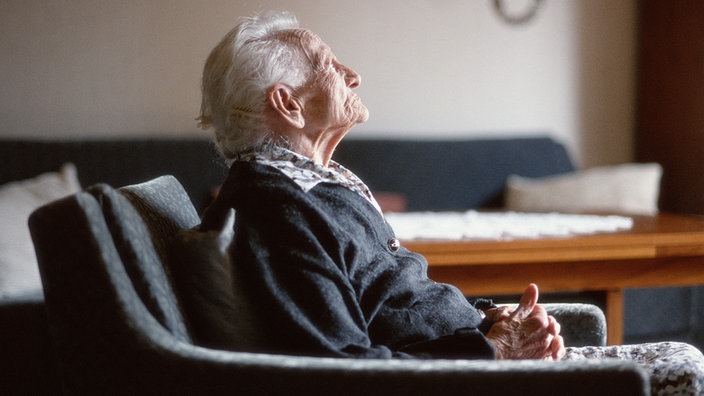 Eine alte Frau sitzt nachdenklich in einem Sessel