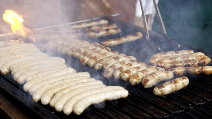 Bratwürste liegen auf dem Grill. Rauch steigt auf.