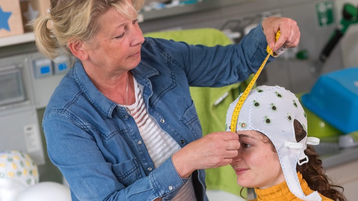 Eine Frau bereitet eine Probandin für ein Elektroenzephalogramm vor