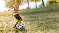 Ein Junge spielt freudig mit einem Ball auf einer Wiese.