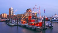 Ein rotes Feuerschiff und einige Ausflugsboote vor der Silhouette der Hafencity.