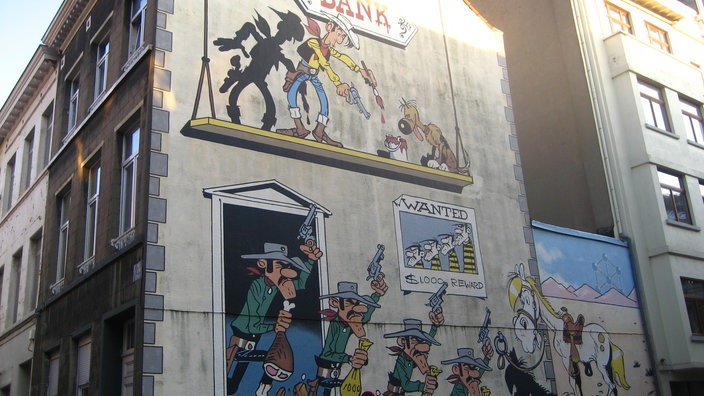 Auf der Seitenwand eines Hauses ist eine Szene aus Lucky Luke aufgemalt. Die Daltons fliehen nach einem Banküberfall, Lucky Luke zielt auf sie.