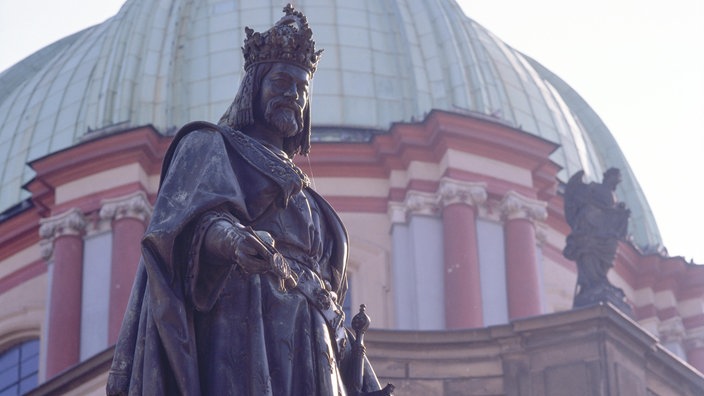 Die Statue Kaiser Karls steht im Vordergrund, im Hintergrund ist ein historischer Kuppelbau zu sehen.