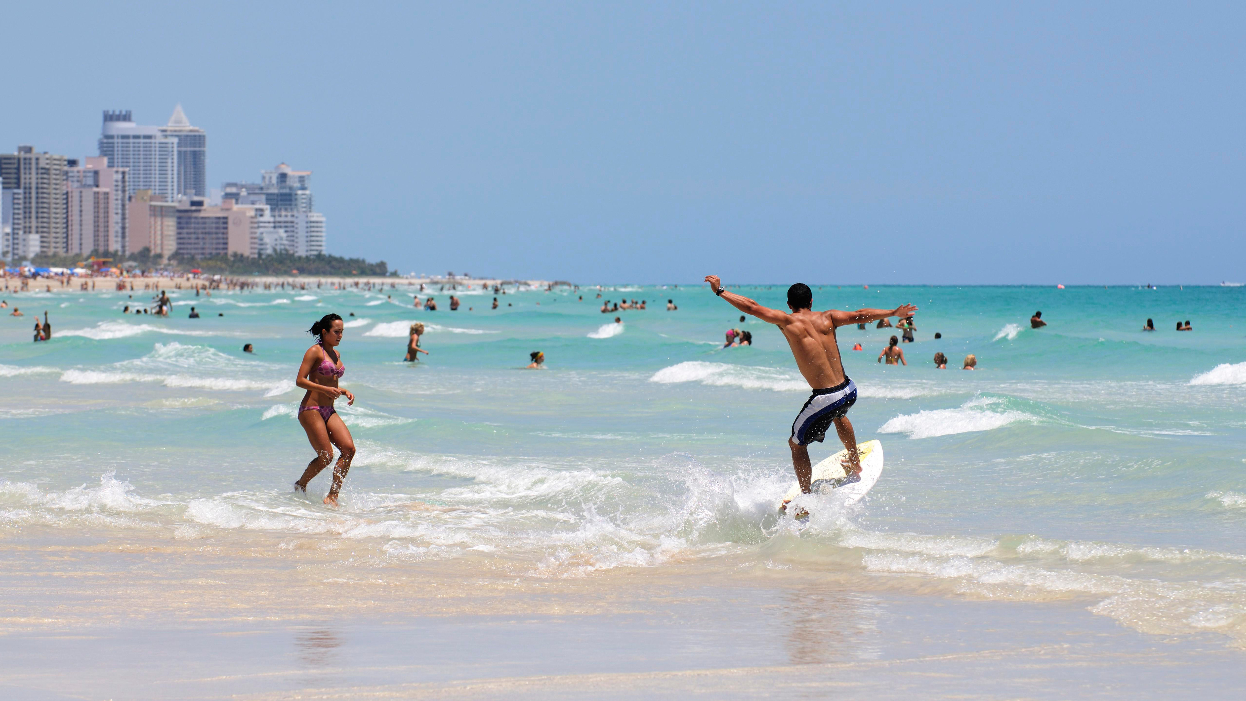 Urlauber am Strand von Miami. Im Hintergrund sieht man die mehrstöckigen Hochhäuser der Stadt.