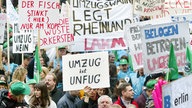 Auf dem Foto sieht man viele Menschen mit Plakaten gegen den Umzug demonstrieren. Auf den Plakaten kann man unter anderem 'Umzug ist Unfug' und 'Umzugswahn legt Rheinland lahm' lesen.