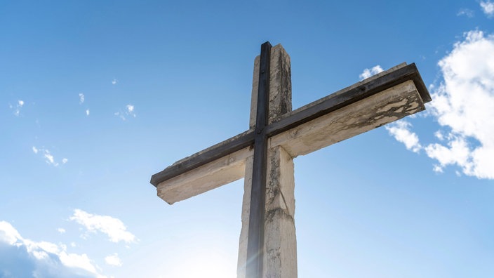 Kreuz aus Stein vor blauem Himmel