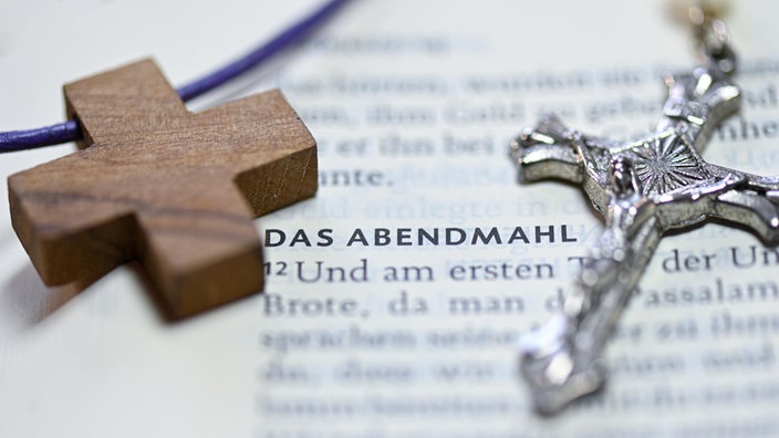 Ein Holzkreuz und ein Kruzifix neben dem Wort "Abendmahl" in einer Bibel 