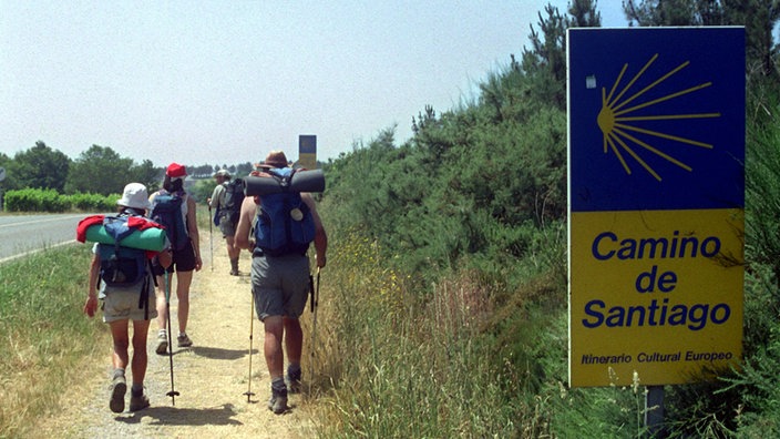 Pilger passieren ein Hinweisschild des Jakobsweges.