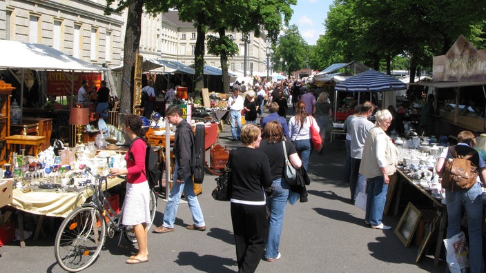 Passanten bummeln an einem Sommertag über einen Flohmarkt und begutachten die Stände