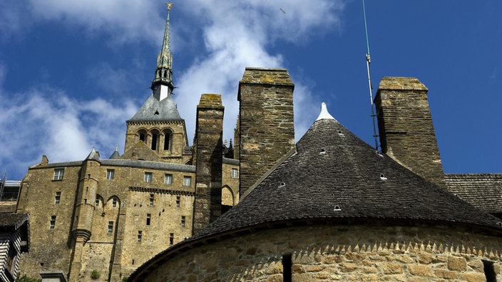 Blick von unten über mächtige Festungsanlagen auf die Kirchturmspitze des Mont St. Michel.