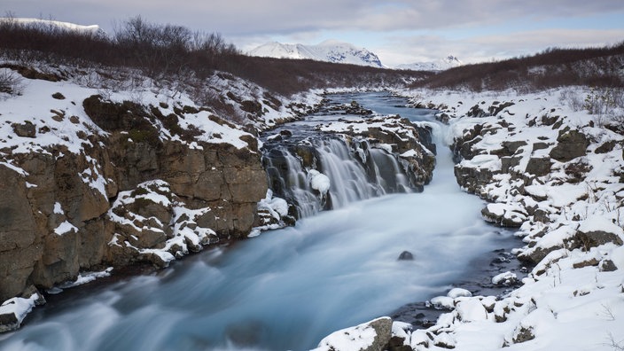 Gebirgsfluss, dessen Ufer verschneit sind