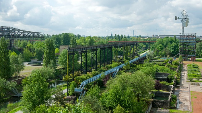 Eine Parkanlage mit Bäumen, Sträuchern, Wasserbecken und Stahlkonstruktionen.