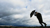 Mann mit Regenschirm vor Gewitterwolken