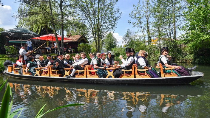 Ein Boot mit Ausflüglern in traditioneller Tracht fährt über einen kleinen Kanal.