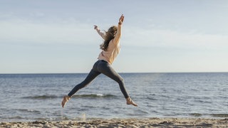 Eine Frau macht Luftsprünge am Strand 