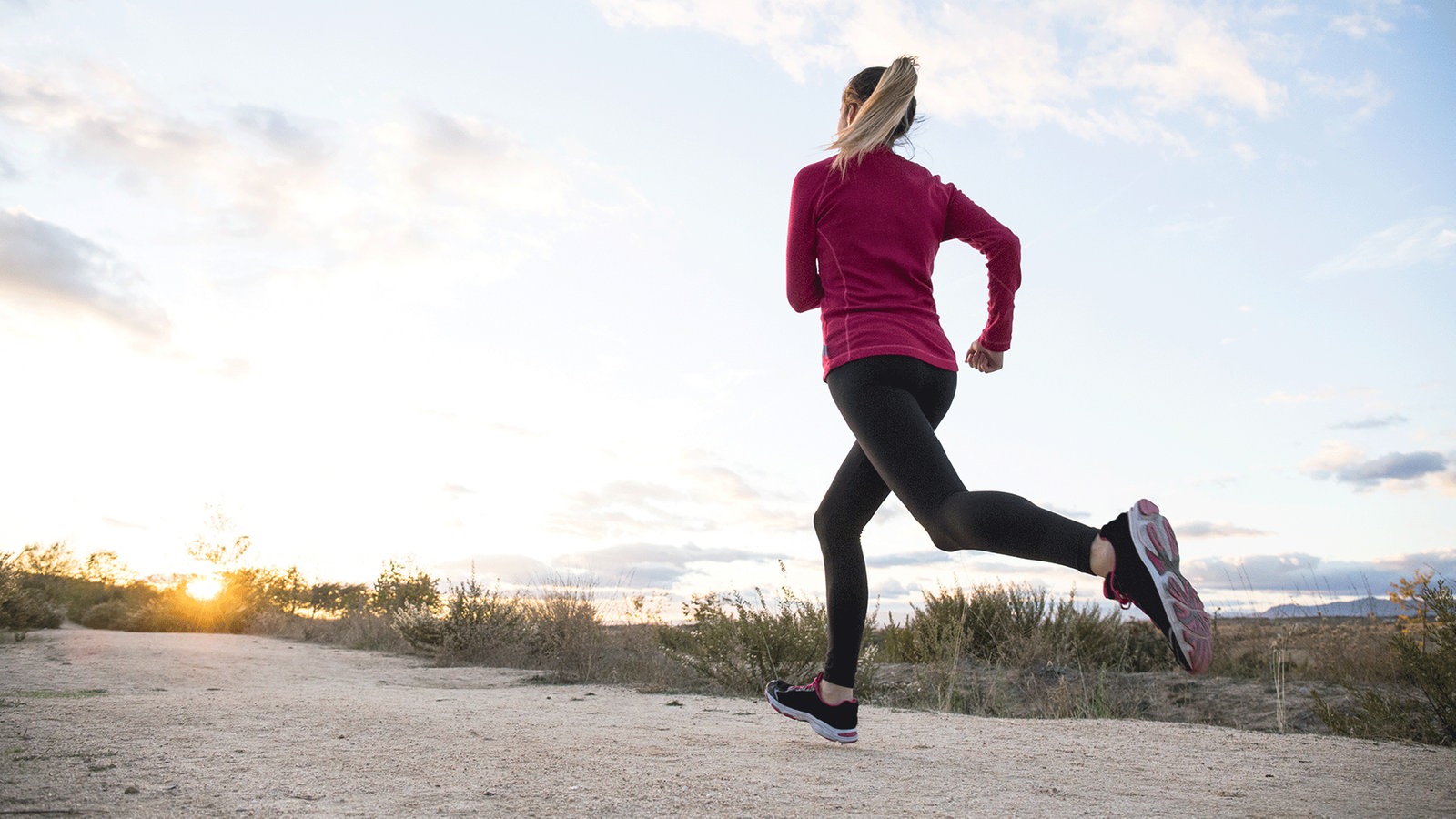 Eine Frau joggt in Sportkleidung auf sandigem Boden.