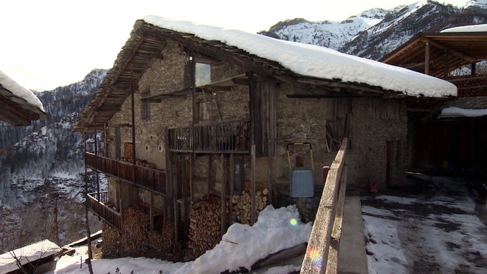 Altes Steinhaus mit schneebedecktem Holzdach in den Bergen.