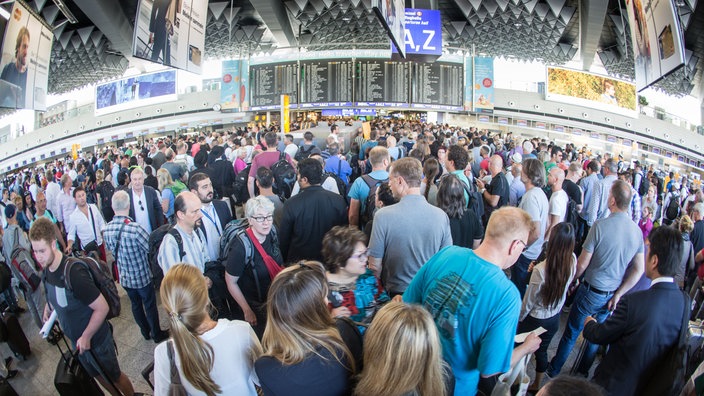 Viele Menschen stehen mit Koffern in einer Flughafenhalle