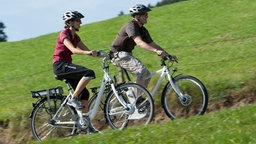 Mann und Frau fahren mit Pedelecs einen Berg hoch 